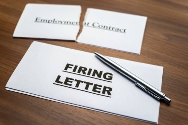 Torn employment contract, and next to it a firing letter, on a wooden surface. clipart