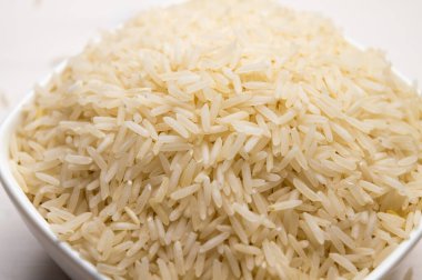 Çiğ basmati pilavı, beyaz kâse içinde, hafif ahşap yüzey üzerinde..