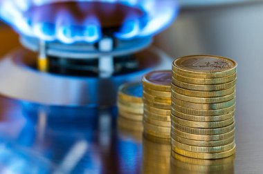 Gas stove lit, with stacks of coins above it. Increase in gas costs and tariffs. clipart