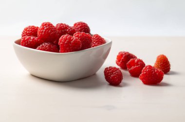 Beyaz bir kasede kırmızı bir peçetenin üzerinde olgun ahududular. Ahududu ekimi ve kullanımı.