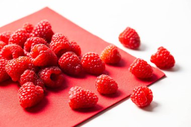 Beyaz bir kasede kırmızı bir peçetenin üzerinde olgun ahududular. Ahududu ekimi ve kullanımı.