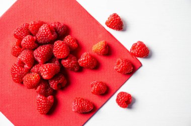 Beyaz bir kasede kırmızı bir peçetenin üzerinde olgun ahududular. Ahududu ekimi ve kullanımı.