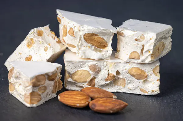 Sert nougat parçaları, yanında bademler, koyu bir levha yüzeyinde.