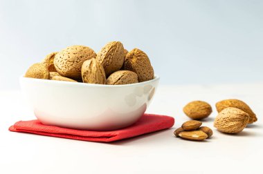 Almonds in white bowl, next to shelled almonds, on white wooden surface. clipart