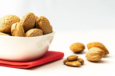 Almonds in white bowl, next to shelled almonds, on white wooden surface. clipart