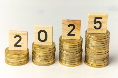Yığınla bozuk para ve 2025 rakamını heceleyen tahta küpler. Yeni yıl, ekonomi ve zenginlik.