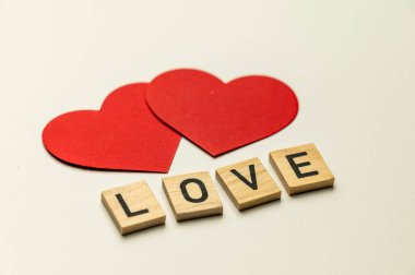 Aşk kelimesi, tahta karelerle bembeyaz bir yüzeyde, kırmızı kalplerin yanında..