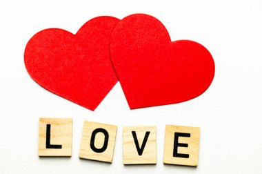 Aşk kelimesi, tahta karelerle bembeyaz bir yüzeyde, kırmızı kalplerin yanında..