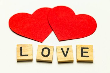 Aşk kelimesi, tahta karelerle bembeyaz bir yüzeyde, kırmızı kalplerin yanında..