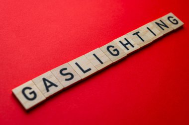 Sözcük Gaslighting, kırmızı yüzeyde tahta alfabe bloklarıyla yazılmış..