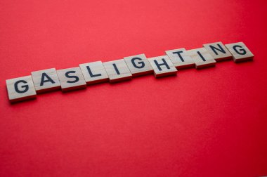 Sözcük Gaslighting, kırmızı yüzeyde tahta alfabe bloklarıyla yazılmış..