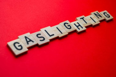 Word Gaslighting, written with wooden alphabet blocks, on red surface. clipart