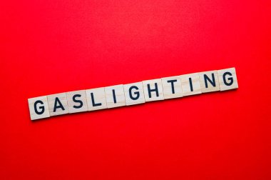 Sözcük Gaslighting, kırmızı yüzeyde tahta alfabe bloklarıyla yazılmış..