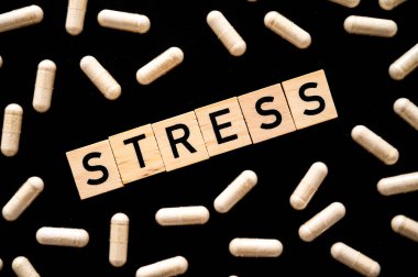 Sözcük stresi, siyah arkaplanda tahta alfabeyle ve tıbbi tabletlerin etrafında oluşmuş. Kaygının özeni.