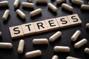 Sözcük stresi, siyah arkaplanda tahta alfabeyle ve tıbbi tabletlerin etrafında oluşmuş. Kaygının özeni.