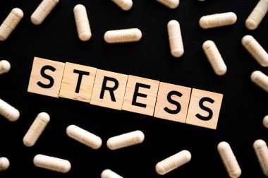 Sözcük stresi, siyah arkaplanda tahta alfabeyle ve tıbbi tabletlerin etrafında oluşmuş. Kaygının özeni.