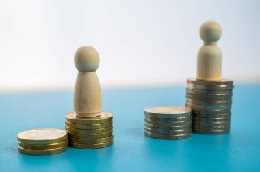 Kadınlar ve erkekler arasındaki iş yerinde eşit ücret kavramı. Bozuk para yığınları üzerinde tahta figürler.