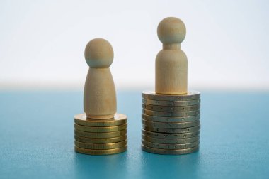 Kadınlar ve erkekler arasındaki iş yerinde eşit ücret kavramı. Bozuk para yığınları üzerinde tahta figürler.