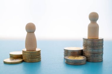 Kadınlar ve erkekler arasındaki iş yerinde eşit ücret kavramı. Bozuk para yığınları üzerinde tahta figürler.