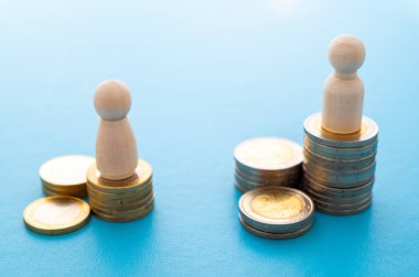 Kadınlar ve erkekler arasındaki iş yerinde eşit ücret kavramı. Bozuk para yığınları üzerinde tahta figürler.