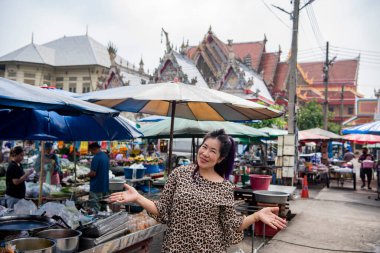 Thailand, Nakhon Pathom - November, 11, 2023: Asian woman posing against market at Wat Klang Bang Kaeo in Tambon Nakhon Chaisi Village near city and Province Nakhon Pathom in Thailand.   clipart