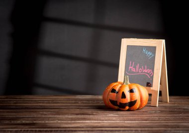 Halloween pumpkin head jack lantern and a chalkboard on wooden 