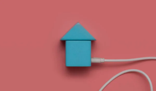 Toy house with electric cable on a pink background,expensive electricity, saving electricity