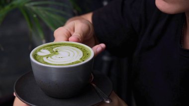 A beautiful young woman enjoys drinking delicious matcha tea with green foam. An invigorating morning drink that energizes for the whole day. Replacing coffee with a healthy matcha.