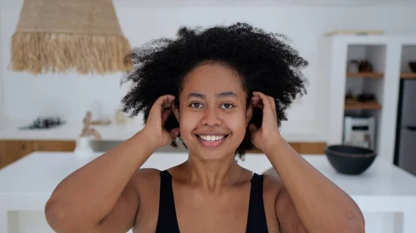 A positive African American woman with thick black wavy hair looks into the frame and straightens her Afra hairstyle. A mixed race woman smiles sweetly into the frame. Beautiful black woman model.