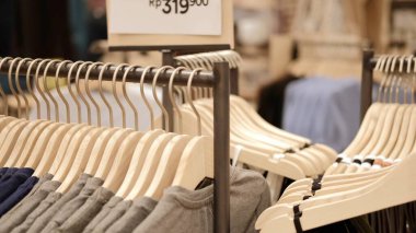 Close-up of hangers with clothes in a store, clothes for sale hang on wooden hangers, a new collection of clothes in different sizes. Industry in the field of clothing trade of famous brands.