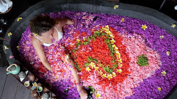 Beautiful woman in a bath with flowers relaxes in a spa hotel. Aroma therapy concept with flowers. Romantic holidays with flowers in the bathroom on vacation in Bali in a paradise island.