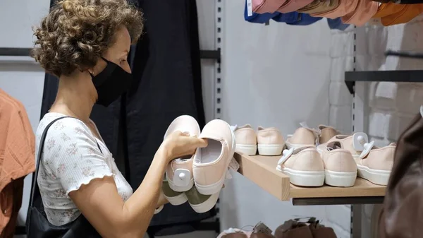 架子上的架子上摆着女鞋 运动鞋 戴面具的购物者做出选择 不同颜色 不同尺寸 有白色橡胶底的鞋子 免版税图库图片