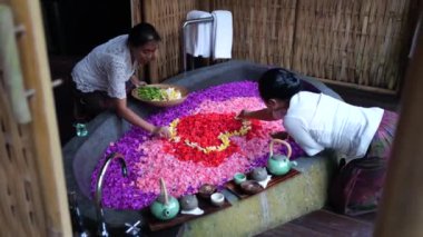 Spa otelindeki çalışanlar banyoyu hazırlar, çeşitli renklerde çiçek yapraklarıyla doldurur ve yaprakları kalp şeklinde suya sererler. Cennette dinlen. Ubud - Endonezya - 2022.