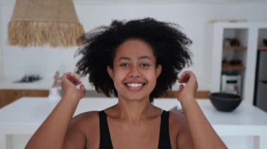 A positive African American woman with thick black wavy hair looks into the frame and straightens her Afra hairstyle. A mixed race woman smiles sweetly into the frame. Beautiful black woman model.