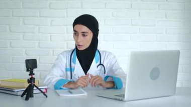A Muslim woman professor of medicine in a hijab conducts training at the university, remotely gives a lecture for future doctors, uses a webcam and a laptop. Fight for the rights of Muslim women.