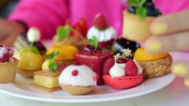 Close-up slow motion shot of a womans hand with a bright yellow manicure, she puts a blackcurrant cake on a large white plate with berry sweet desserts.