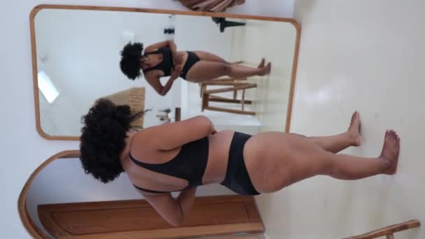 黒のランジェリー姿の鏡の前に黒の女性がぽっちゃりとした姿を見て体が好きだという垂直映像 肥満のアフリカアジア女性の受け入れ — ストック動画
