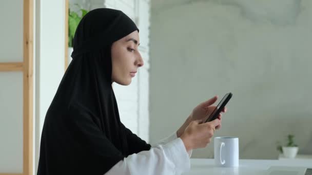 Muslim Woman Bright Cozy Room Sits Carefully Scrolls Information Phone — Stockvideo