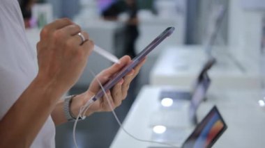 Close-up in the hands of the buyer a stylus and a tablet, touching the stylus to the screen of the tablet. A woman uses a stylus to check the screen of a graphics tablet. Ubud - Indonesia - 2022.
