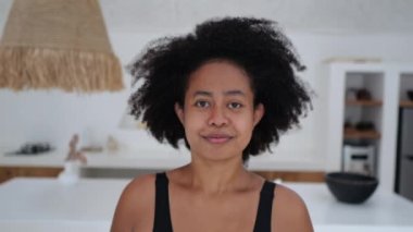 Beautiful African American woman with thick black wavy hair. A mixed race woman smiles sweetly into the frame. Attractive black female model looking at the camera with a snow-white smile.