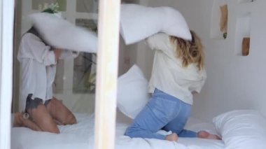 Two young women on the bed had a pillow fight after the fight hugging for peace. Friendly games with friends. Funny pastime on vacation in bed. Friends live happily together.