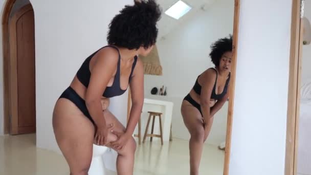 黒いランジェリーを着たアフリカ系アジア人女性は鏡の前でセルライトを調べ 彼女の体がこんなに太ったとは信じられない 世界中のファーストフードを食べている肥満の女性 — ストック動画
