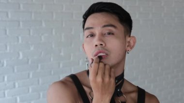 The passionate face of a handsome homosexual man who paints his lips with lipstick. LGBT community for the rights of sexual minorities. Asian model male gay transgender looking at the camera.