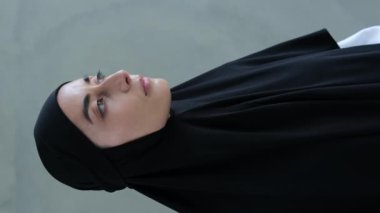 Siyah tesettürlü bir Arap kadının dikey videosu. İslam dünyasının dindar fanatikleri kadınları meraklı erkek gözlerinden saklanmak için başörtüsü takmaya zorluyor..