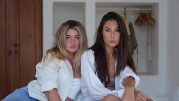 两个朋友并排坐在床上的卧室里 凝视着镜框 真正的女性友谊 女性可以互相信任 与所有的秘密 两个女朋友一起站在摄像机前 — 图库视频影像