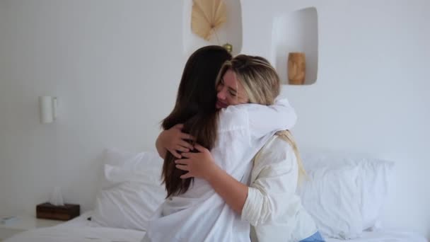 寝室のベッドの上の親友のフレンドリーな抱擁 ブルネットとブロンドの2人の女性が抱き合って座っている 彼らはお互いを愛しているので 友人は互いにしっかり抱擁します女性の友情の概念 — ストック動画