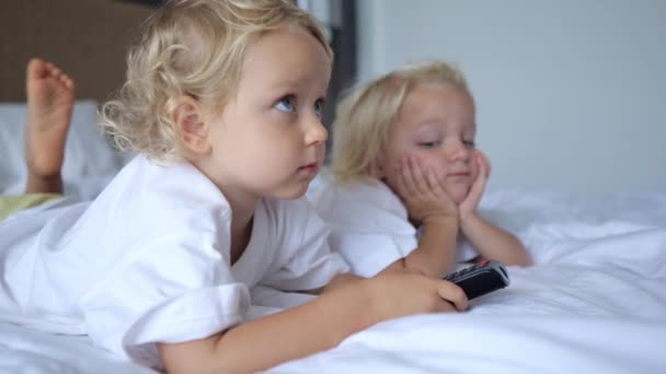 Małe Bliźniaczki Leżą Dużym Łóżku Brzuchu Oglądają Telewizję Wiszącą Ścianie — Wideo stockowe
