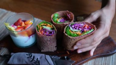 Appetizing vegetarian rolls wrapped in flatbread filled with various vegetables. On a wooden plate, a healthy breakfast of a vegetable dish and a drink with fruits and berries. Delicious vegan.