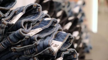 Close-up of a huge range of jeans in different sizes and styles for men and women in a large clothing store. Jeans are neatly folded and stacked. Each pair has a size tag.