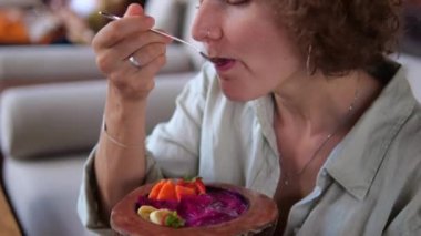 View of a woman who is happy to eat an appetizing dish with fruits and healthy porridge in coconut shell plates in a vegan restaurant. Healthy fruit breakfast served in a trendy vegan restaurant.